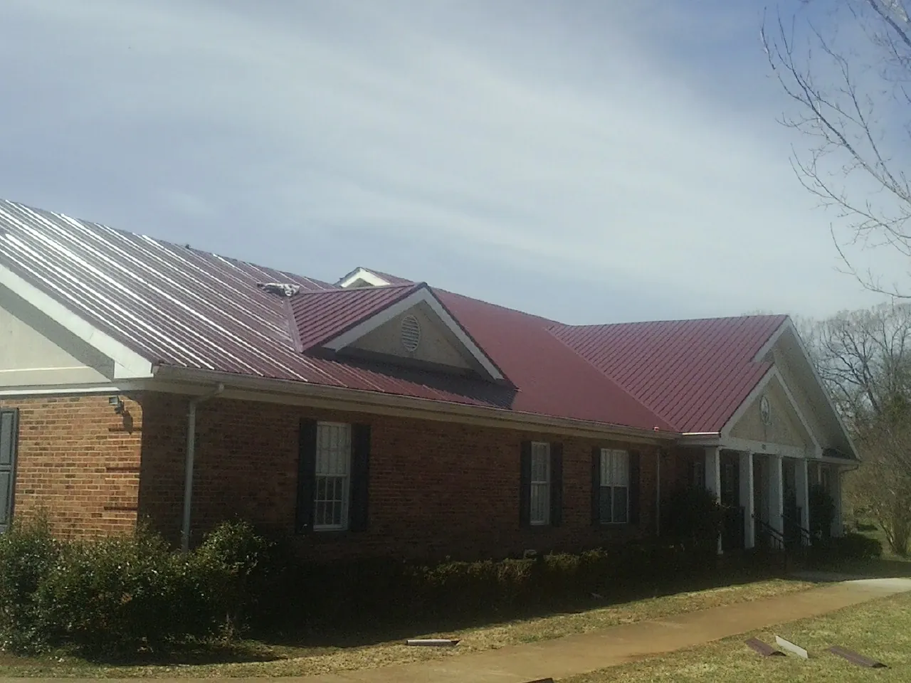Red metal roof with gabled entries on a long brick building, from a Hail Damage Roof Repair job in Sapphire