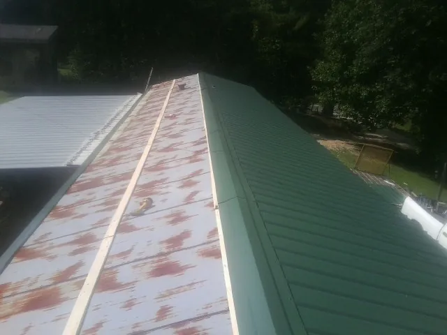 Old rusted panels beside newly installed green metal roofing — Wind Damage Roof Repair by Roofing Brothers in Sapphire