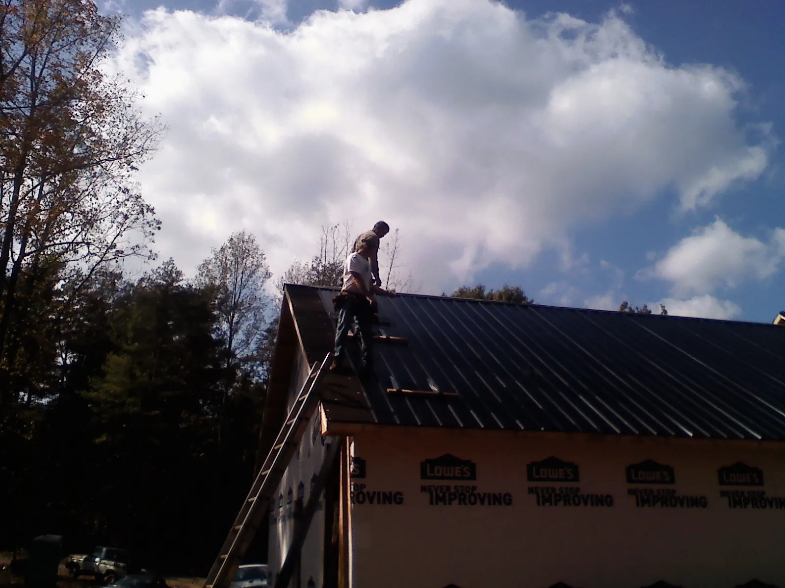 Roofer fastening dark metal panels high against a cloudy sky, from a Roof Inspection job in Sapphire