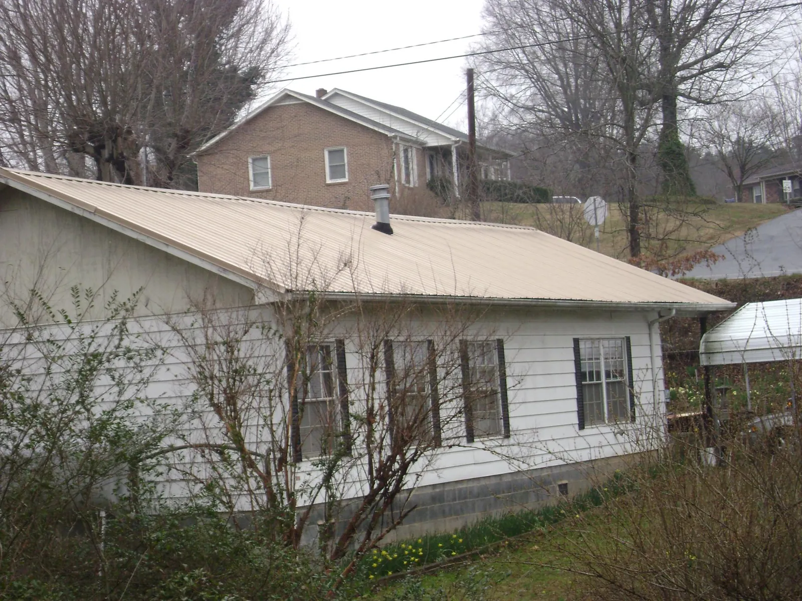 Tan metal roof on a white sided house set into a hillside — Commercial Roofing by Roofing Brothers in Sapphire