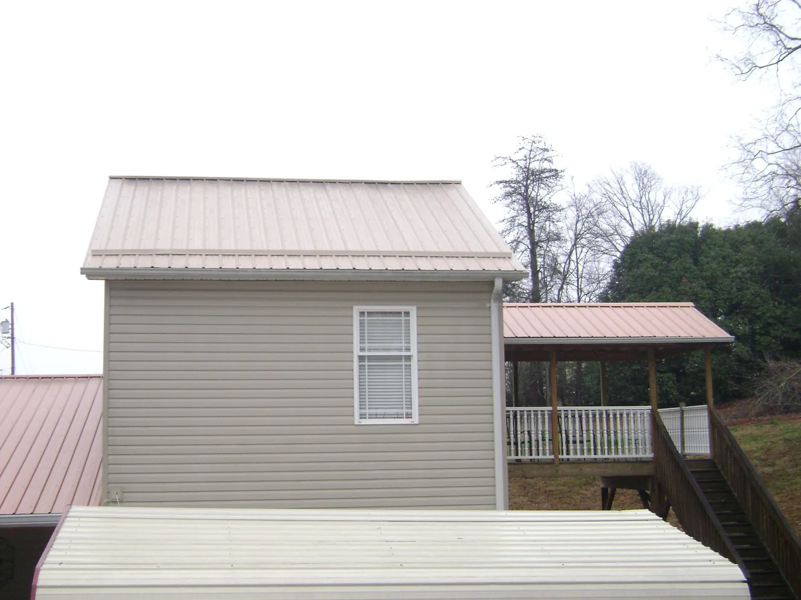 Tan metal roofs on a two story addition and attached porch, from a Roof Replacement job in Sapphire